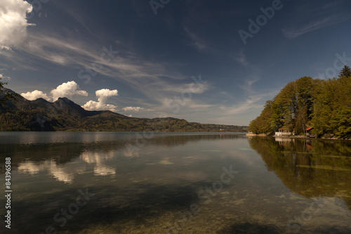 A view on a lake with a small cabin and mountains and clouds in the background