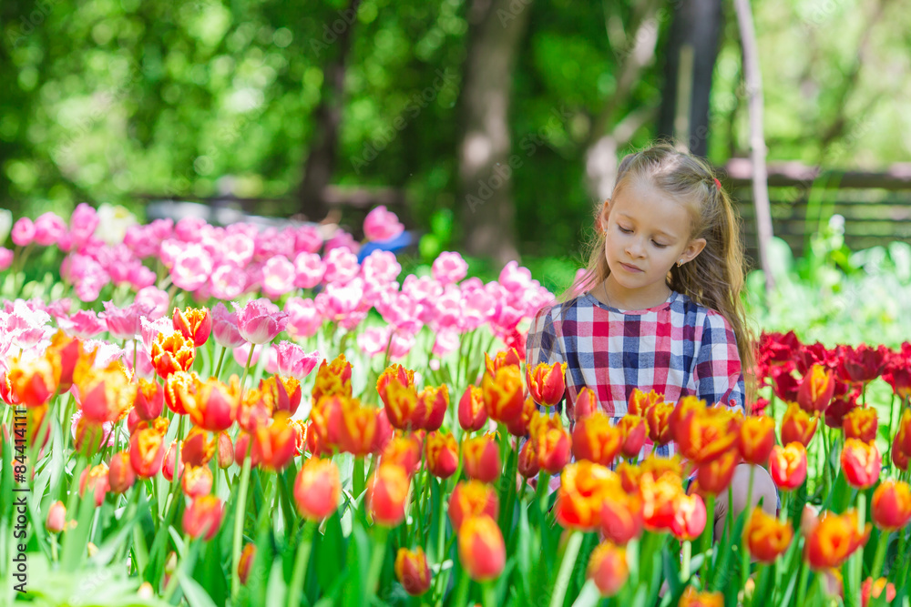 Little adorable girl in the lush garden of tulips