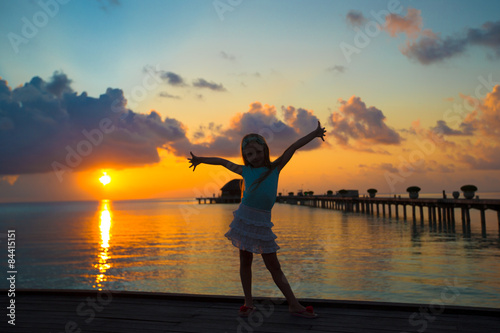 Silhouette of adorable little girl on wooden jetty at sunset