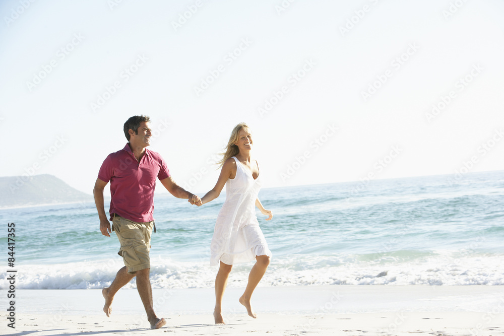 Young Couple Running Along Sandy Beach On Holiday