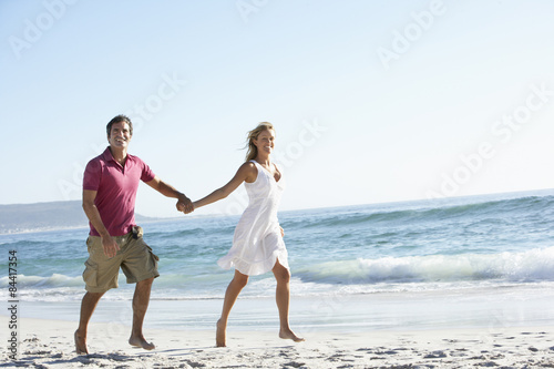 Young Couple Walking Along Sandy Beach On Holiday