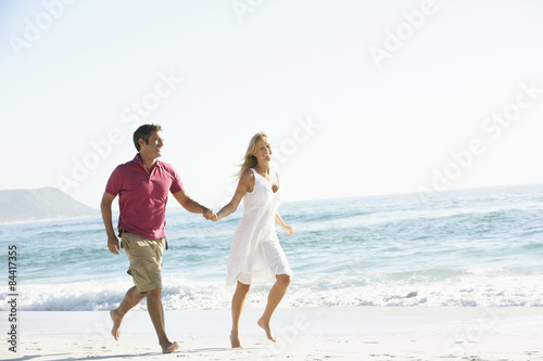 Young Couple Running Along Sandy Beach On Holiday