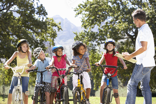 Group Of Children Having Safety Lesson From Adult Whilst Riding Bikes In Countryside