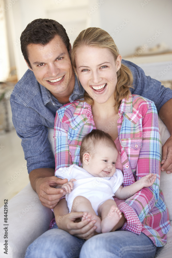 Young Family With Baby Relaxing On Sofa At Home