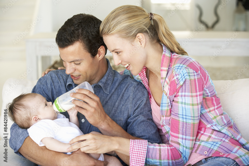 Young Family With Baby Feeding On Sofa At Home Young Family With Baby Feeding On Sofa At Home