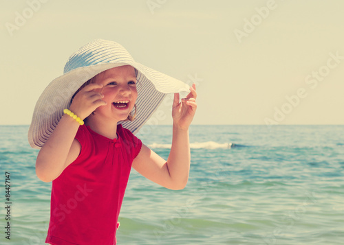 Funny little girl in a big hat on the beach. The image is tinted