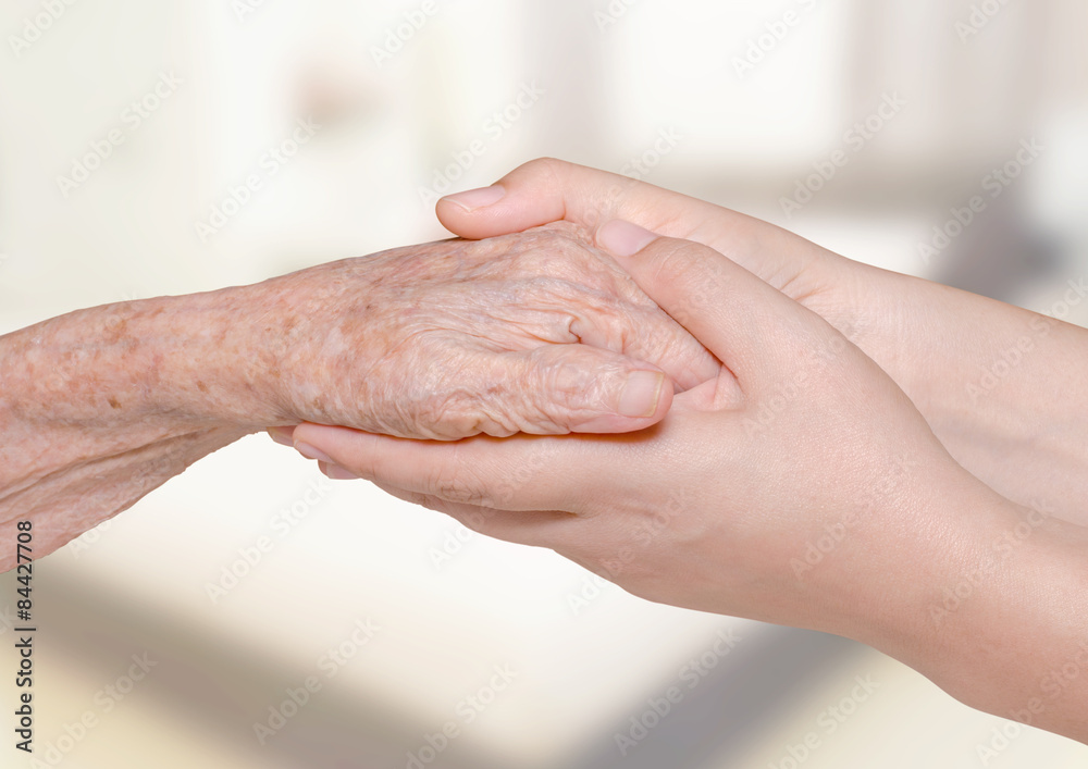 Fototapeta premium Young woman holding her grandma hand in bedroom