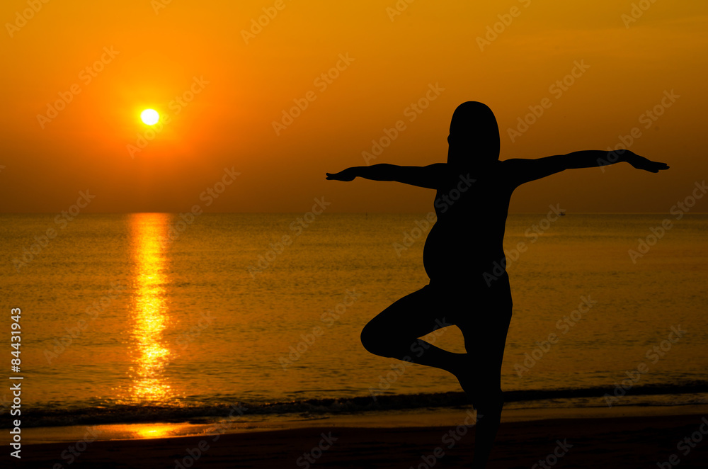 Silhouette of pregnant doing yoga on the beach in morning