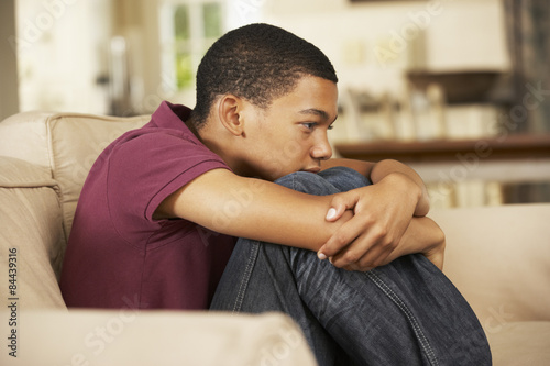 Unhappy Teenage Boy Sitting On Sofa At Home