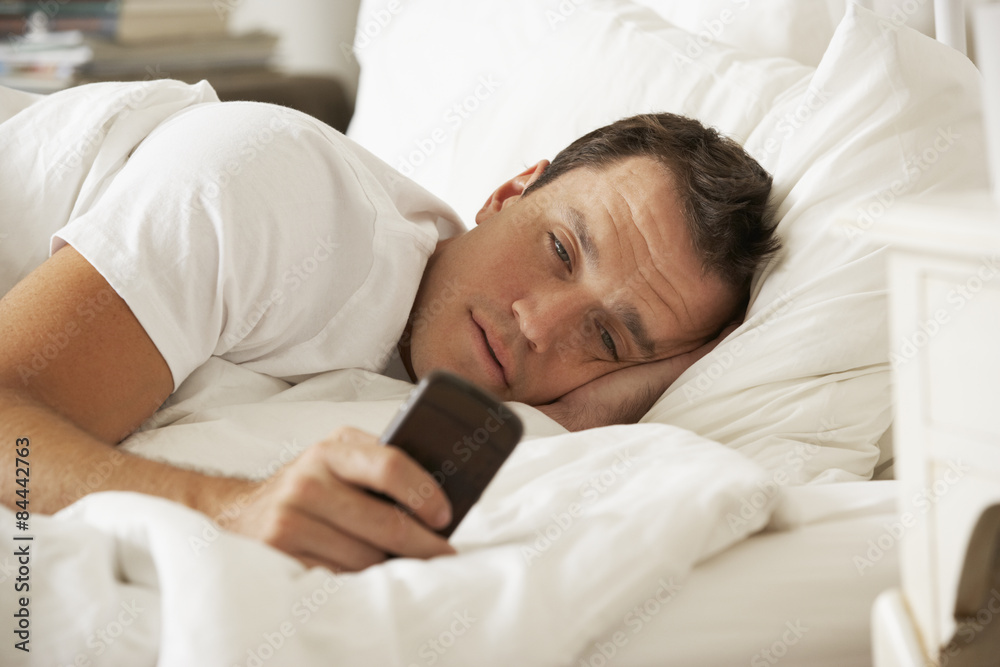 Man In Bed At Home Texting On Mobile Phone Man In Bed At Home Texting On Mobile Phone