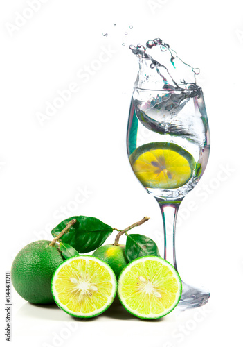 Lime splashing into glass of water on white background