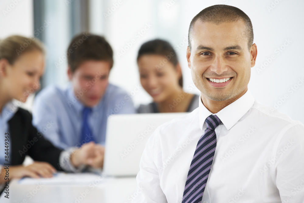 Portrait Of Male Executive With Office Meeting In Background Portrait Of Male Executive With Office Meeting In Background