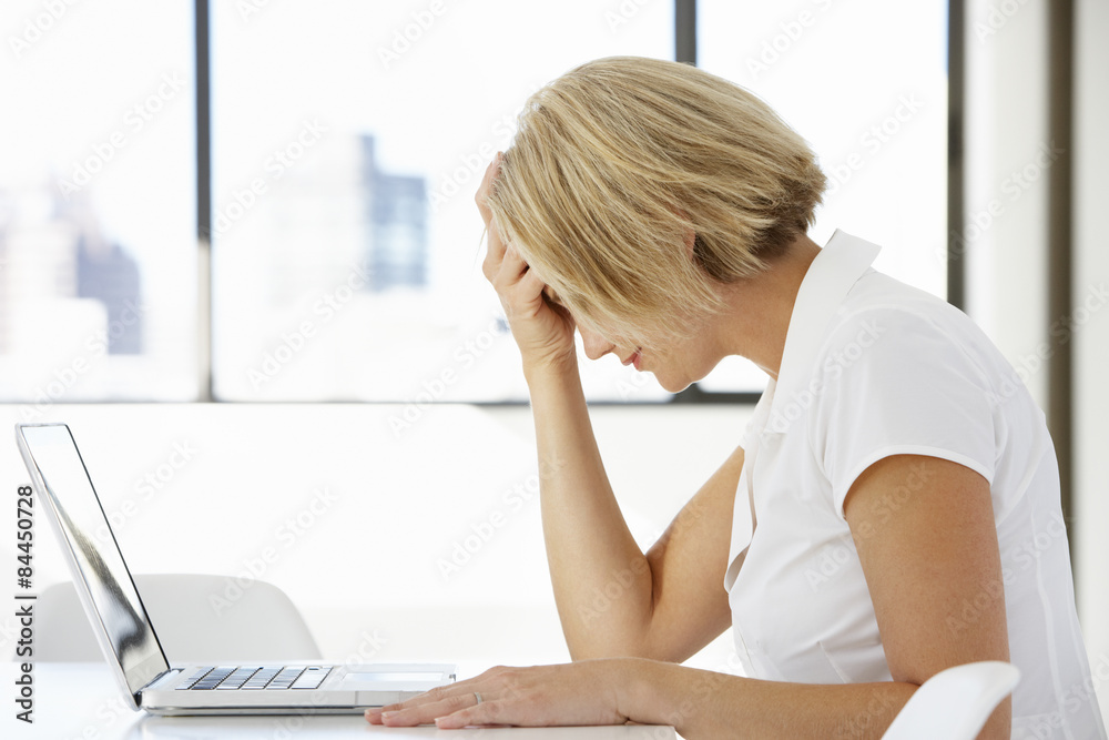 Frustrated Businesswoman Sitting At Desk In Office Using Laptop Frustrated Businesswoman Sitting At Desk In Office Using Laptop