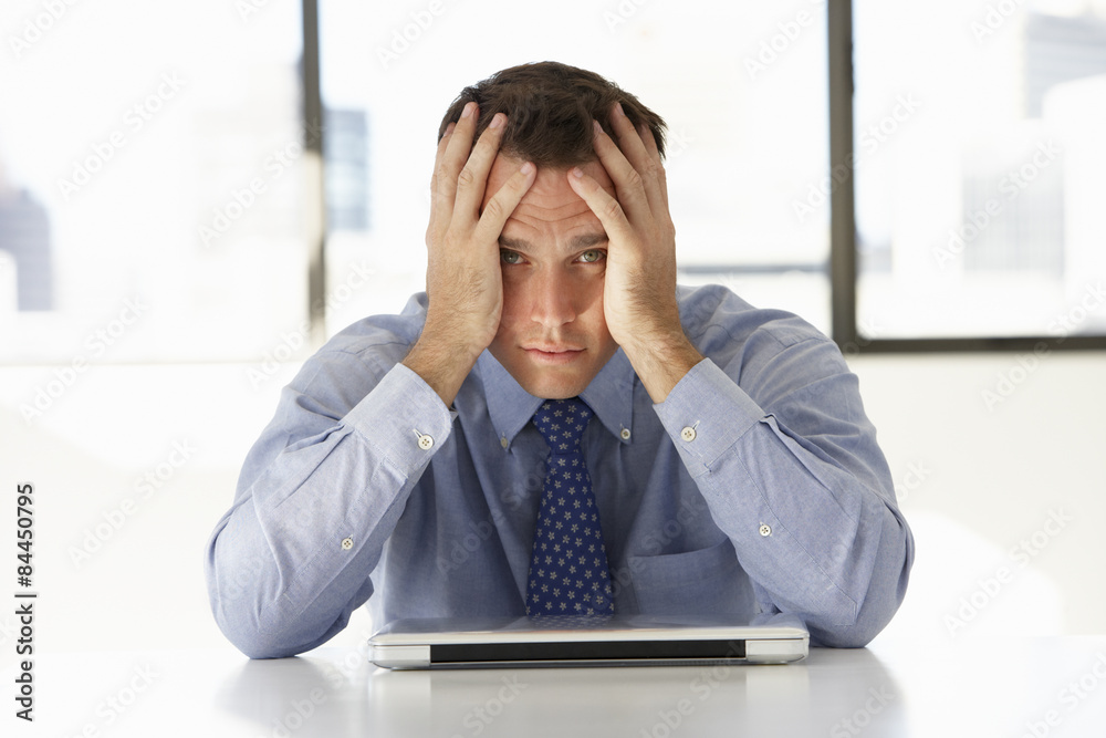 Frustrated Businessman Sitting At Desk In Office Using Laptop Frustrated Businessman Sitting At Desk In Office Using Laptop