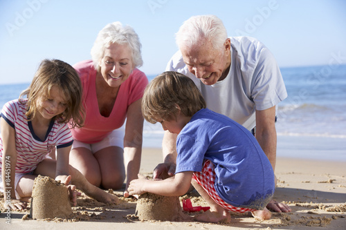 Grandparents And Grandchildren Building Sandcastle On Beach