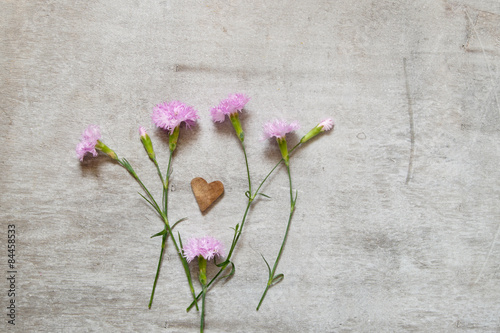 Three carnation flower on a gray background and wooden heart