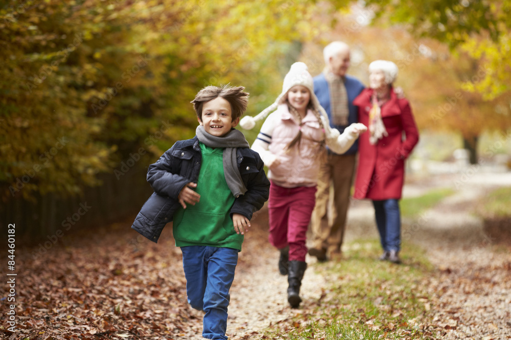 Grandparents With Grandchildren Running Along Autumn Path Grandparents With Grandchildren Running Along Autumn Path