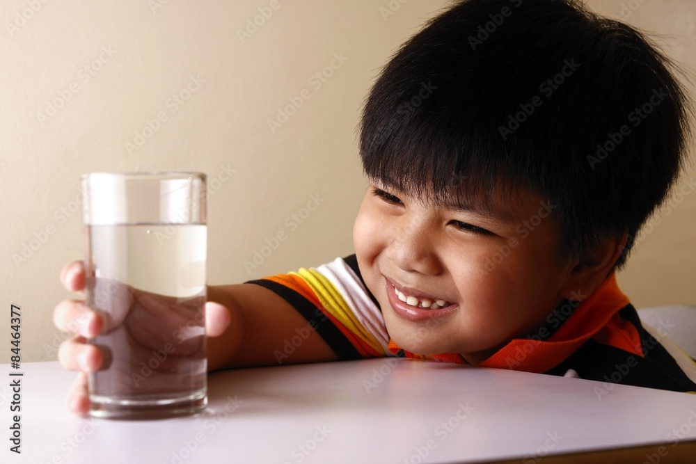 Kid holding a glass of water on a wooden table Kid holding a glass of water on a wooden table