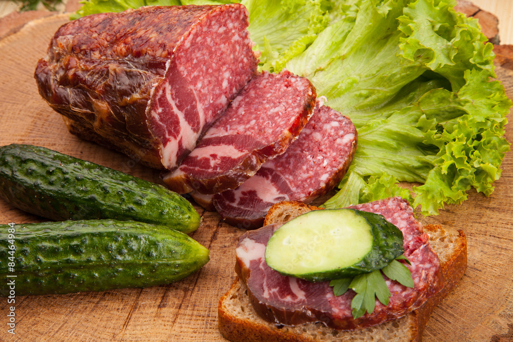 Smoked meat sausage salami with bright summer vegetables and bread on wooden background Smoked meat sausage salami with bright summer vegetables and bread on wooden background