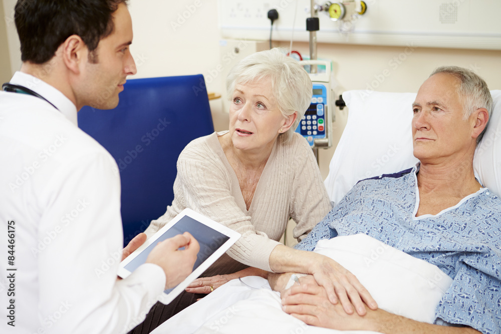 Doctor With Digital Tablet Talking To Couple By Hospital Bed Doctor With Digital Tablet Talking To Couple By Hospital Bed
