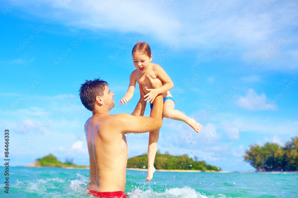 joyful father and son having fun in water on tropical beach joyful father and son having fun in water on tropical beach