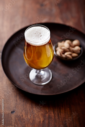 Glass of beer on a rustic tray; salted almonds in background