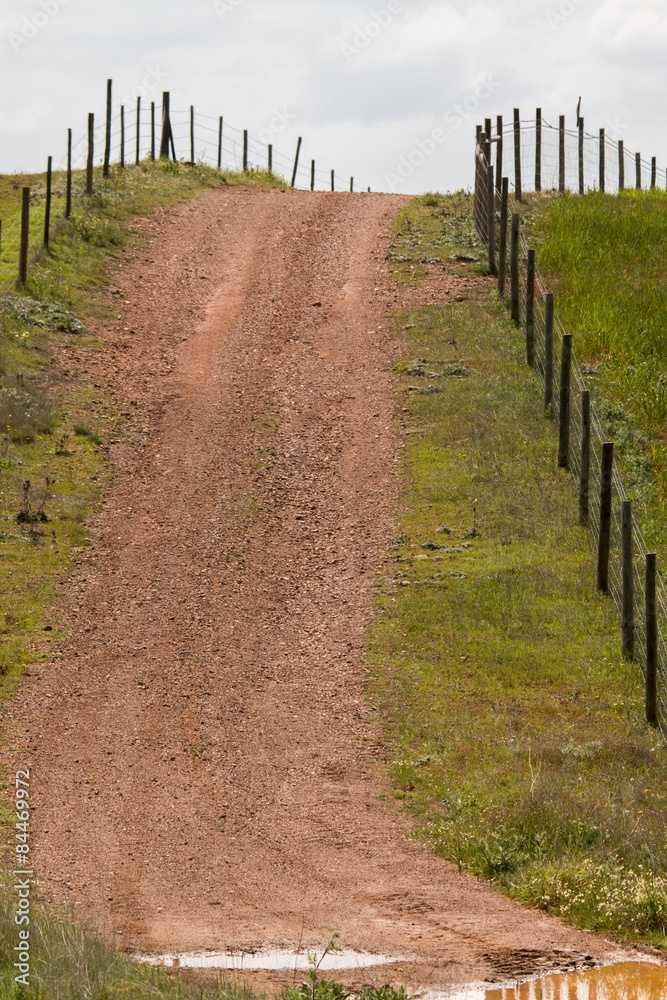Obraz premium View of a hill with a fence and dirt road in Alentejo, Portugal.