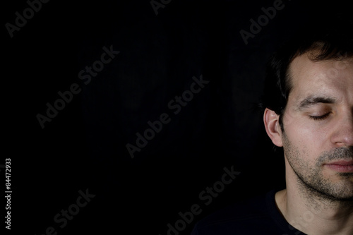 peaceful young man with closed eyes, black background