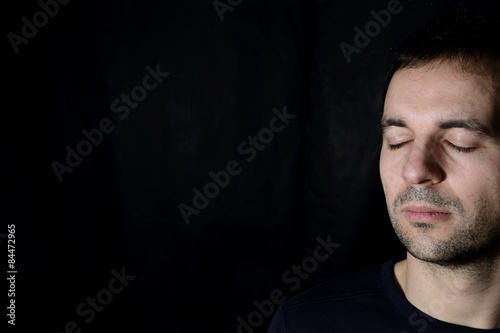 peaceful young man with closed eyes, black background
