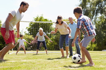Multi Generation Playing Football In Garden Together
