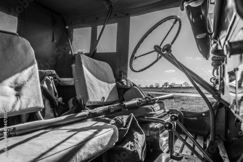 Black and white interior of WW2 Jeep with rifle across seat.