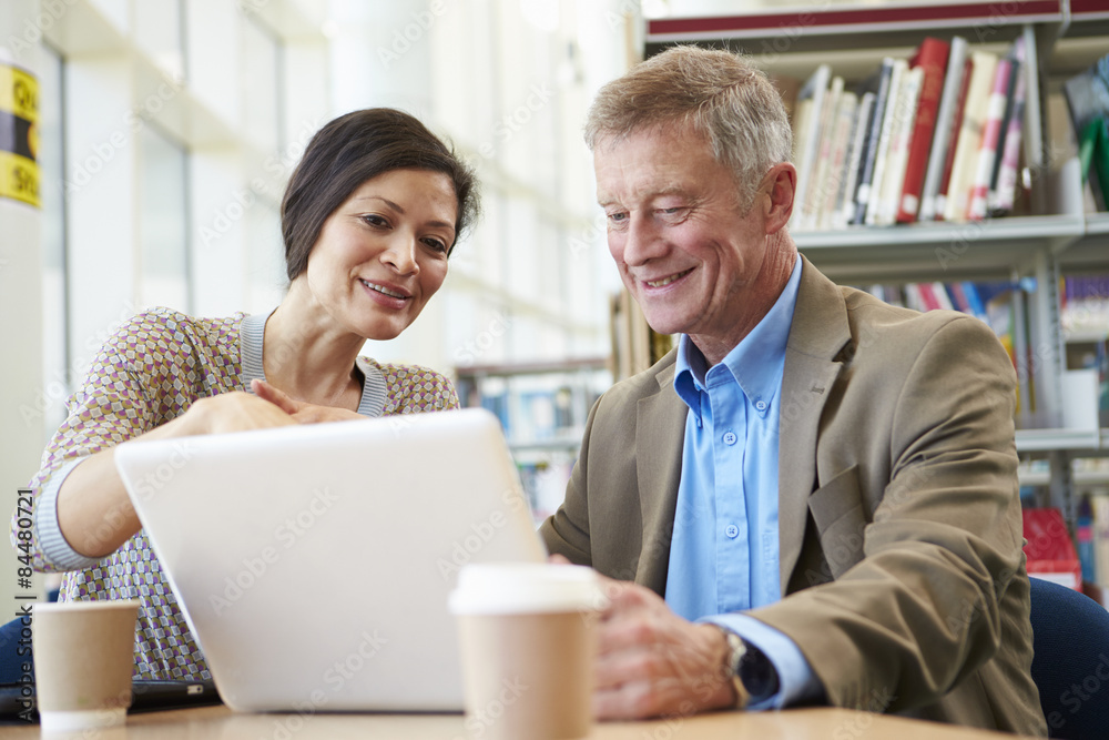 Teacher Helping Mature Student With Studies In Library Teacher Helping Mature Student With Studies In Library