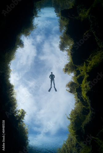 A freediver floats in freshwater under a cloud background over a chasm at Piccaninnie Ponds in South Australia photo