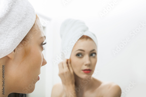 Junge Frau eingewickelt in ein Handtuch schaut in den Spiegel