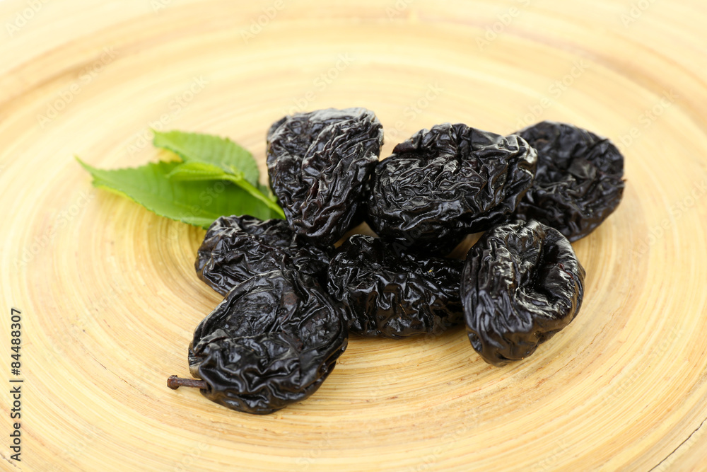 Pile of prunes with leaves on wooden background Pile of prunes with leaves on wooden background