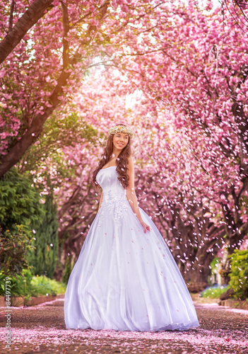 Beautiful bride in a white dress under the sakura tree and flower petals