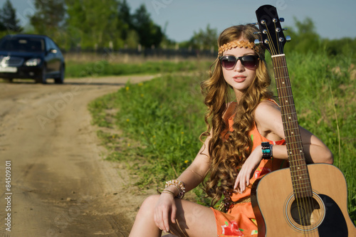 Hippie girl travelling with her guitar on a road