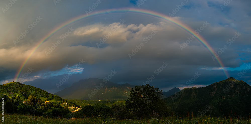 Naklejka premium Real rainbow above a small village in the mountains at sunset