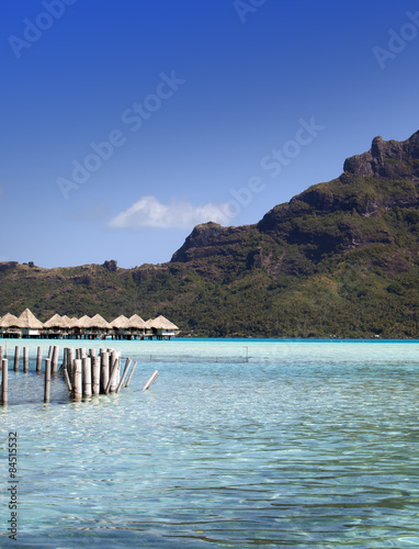 the destroyed thrown huts on water and island with palm trees in the ocean and mountains on a background..