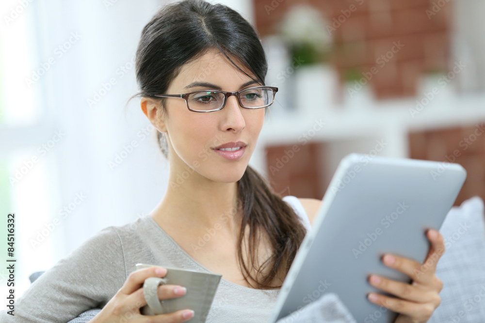 Fototapeta premium Brunette girl relaxing in sofa connected on tablet and drinking hot tea