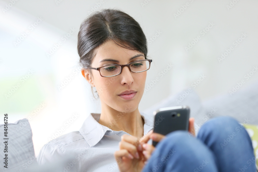 Brunette girl with eyeglasses using smartphone sit in couch Brunette girl with eyeglasses using smartphone sit in couch
