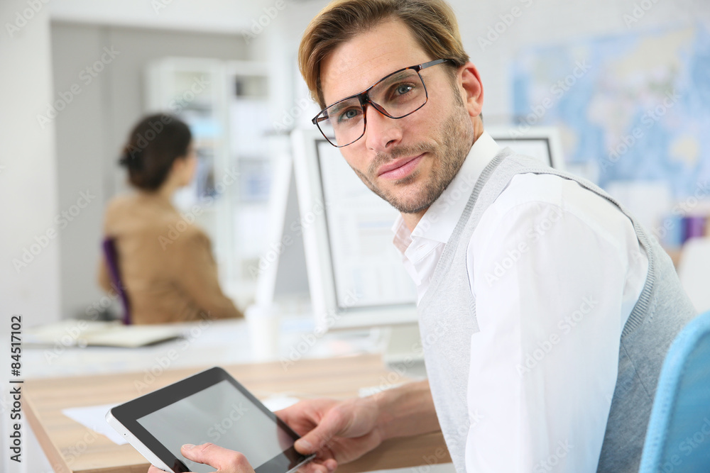 Man in office working on digital tablet, wearing eyeglasses