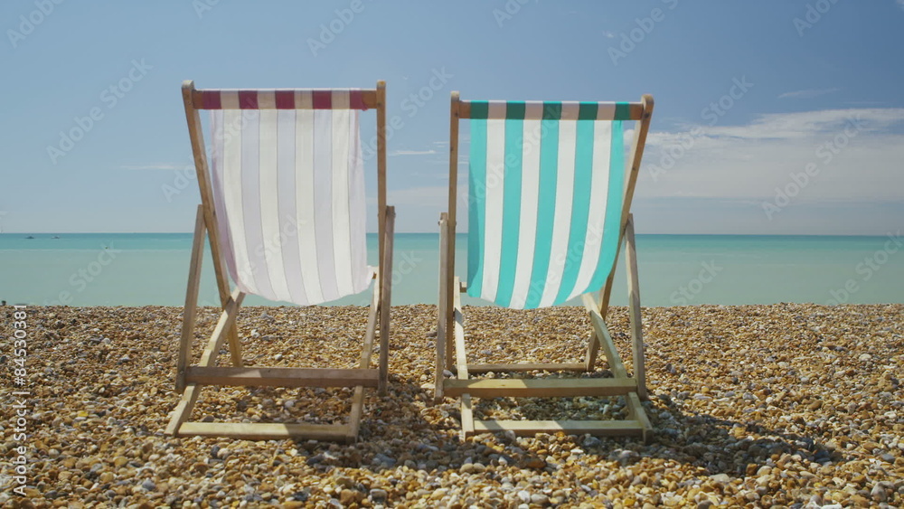 Two empty deck chairs on a pebble beach on a sunny day
