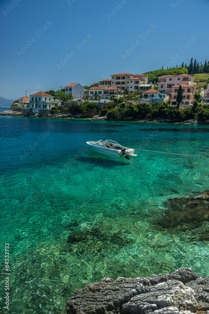 Speedboat moored in turquiose bay in Kephalonia with houses on t