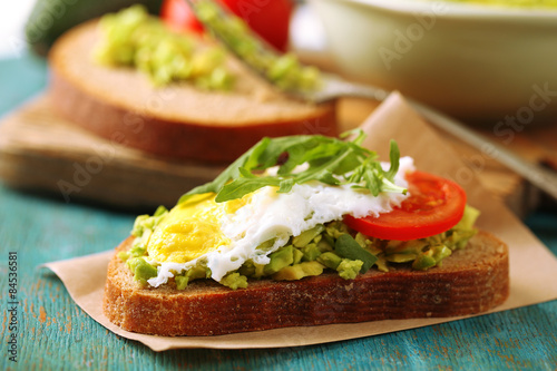 Tasty sandwich with egg, avocado and vegetables on cutting board, on color wooden background