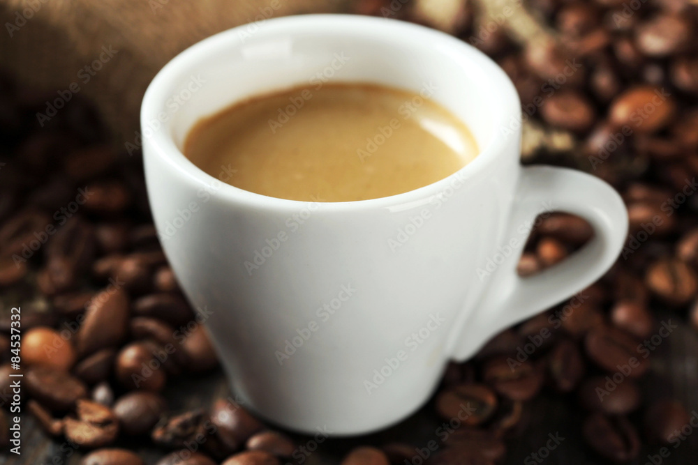 Fototapeta premium Cup of coffee with beans on table close up