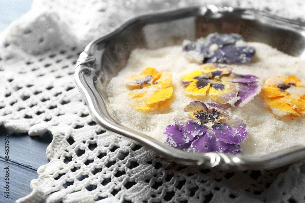 Candied sugared violet flowers on tray, on color wooden background Candied sugared violet flowers on tray, on color wooden background