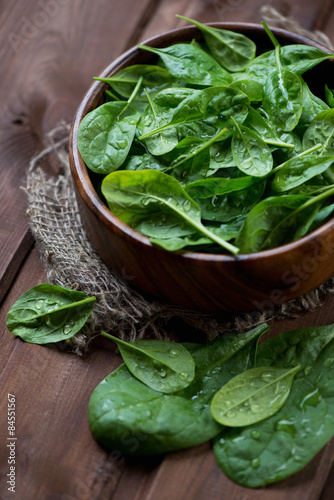Close-up of a wooden bowl with fresh spinach leaves, studio shot