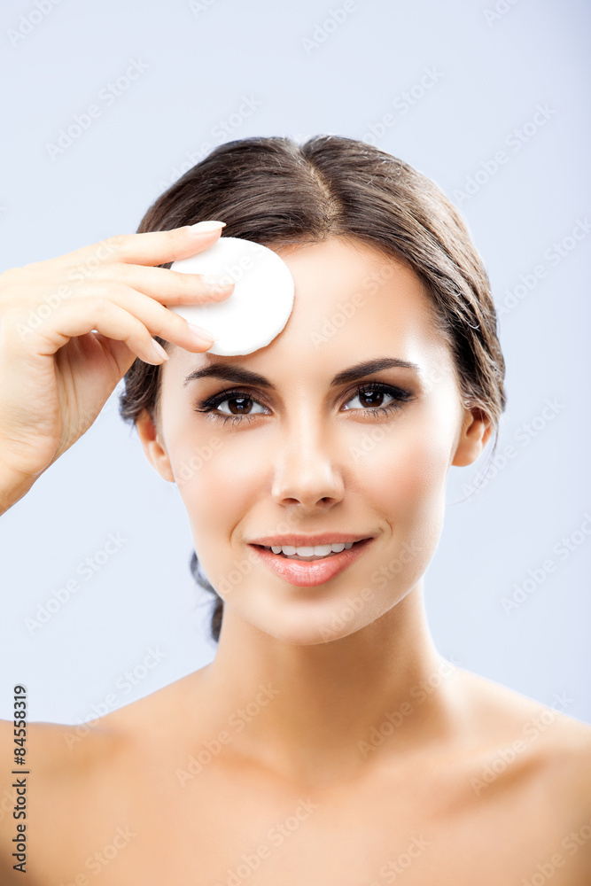 Young woman cleaning skin by cotton pad, over grey