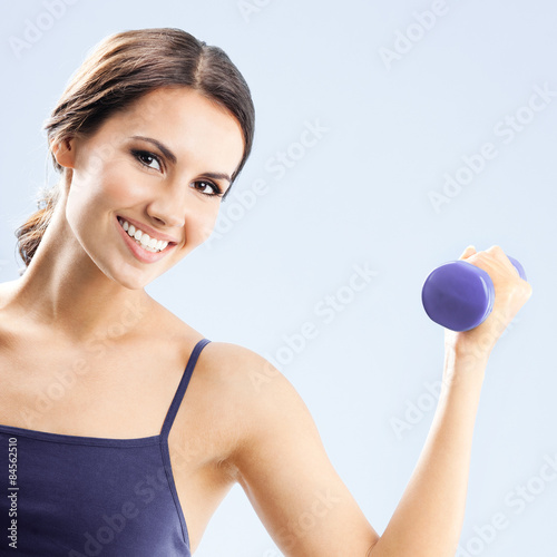 Woman in fitness wear with dumbbell, over grey